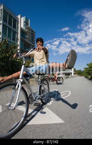 Giovane uomo alza le gambe alto dai pedali durante la guida bike city bike path, Vancouver, British Columbia Foto Stock