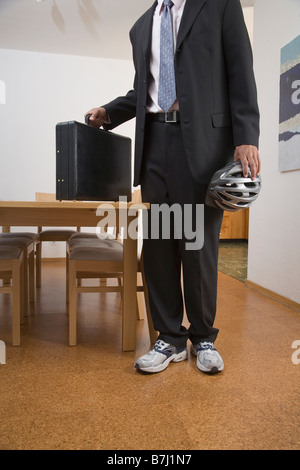 Giovane uomo sul modo di lavorare indossando tuta e scarpe da ginnastica detiene il casco e valigetta Foto Stock