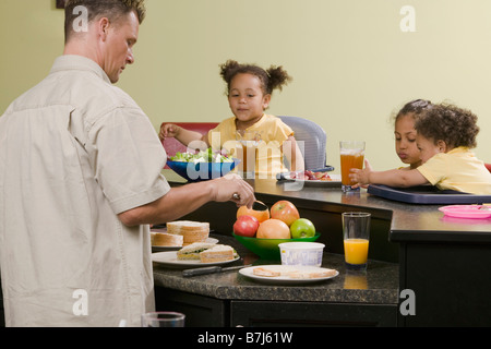 Papà caucasico preparare un pasto per il suo Mulatto bambini, ragazzo 1,5 anni, ragazza di 3 e 6 anni. Foto Stock