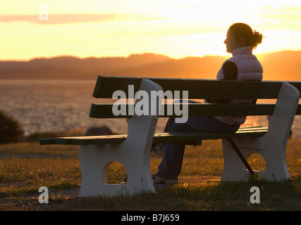 Una donna enoys il tramonto da una panchina nel parco lungo il Victoria's Dallas Road Waterfront Foto Stock