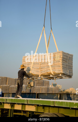 Importazione di materiali da costruzione, operai lo scarico dei pallet di cemento iraniano, consegnati da includersi in corrispondenza della banchina di Al Sharjah, Dubai, UAE Foto Stock