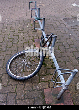 Un danneggiamento della ruota di bicicletta è tutto ciò che è a sinistra di una bicicletta incatenato ad una bici stand Foto Stock