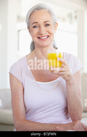 Senior Donna che mantiene il succo di arancia e sorridente alla fotocamera Foto Stock