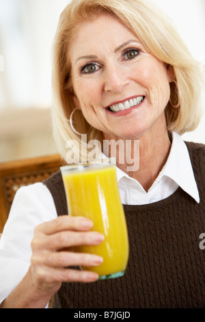 Senior donna bere un bicchiere di succo d'arancia fresco Foto Stock