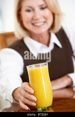 Senior donna bere un bicchiere di succo d'arancia fresco Foto Stock