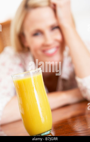 Metà donna adulta guardando un bicchiere di succo d'arancia fresco Foto Stock