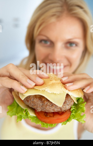 Metà donna adulta tenendo un hamburger, sorridente verso la telecamera Foto Stock