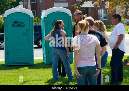 Linea di persone in attesa di utilizzare due toilette portatile esterno su una soleggiata giornata estiva Foto Stock