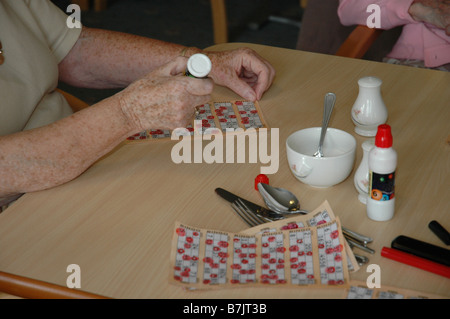 Una donna di mano giocando a bingo con alcune schede e penne a una tabella Foto Stock