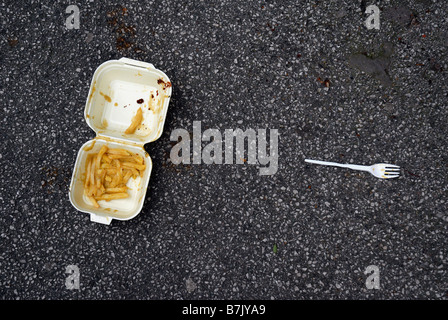 Una plastica scartato il fast food il vassoio contenente un po' di patatine fritte patate scheggiata e una forcella di plastica vicino a terra Foto Stock