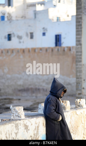 Un uomo è in piedi di fronte della medina di Essaouira indossando un djellaba tradizionale. Foto Stock