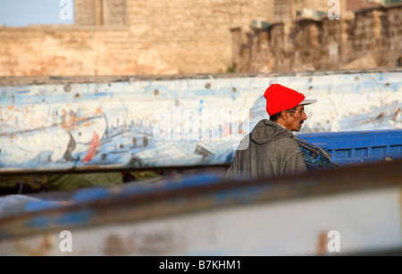 Un pescatore locale sorge accanto alle barche da pesca nel porto di Essaouira Foto Stock