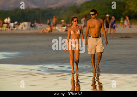 Coppia giovane tenendo le mani mentre passeggiate lungo la spiaggia di Playa Tamarindo, Costa Rica. Foto Stock
