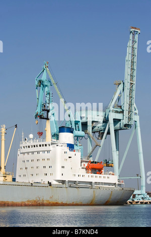 Piccola nave in porto a fianco di gru di contenitore Foto Stock