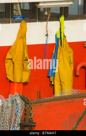 Fishermans giallo impermeabilizza appeso sul retro della timoneria di un commerciale barca da pesca indumenti impermeabili Foto Stock