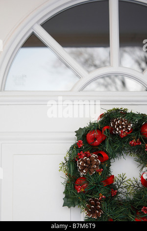 Primo piano di una corona di Natale appesa alla porta bianca anteriore di una casa, nessuno è in verticale Foto Stock