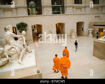 I monaci vestiti di arancione brillante accappatoi, camminando attraverso una galleria di scultura del museo del Louvre a Parigi Francia Europa Foto Stock