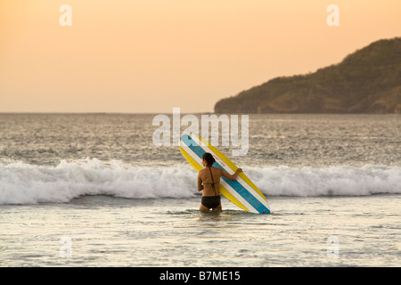 Surfer tenendo la tavola da surf immettendo le onde di Playa Tamarindo, Costa Rica. Foto Stock