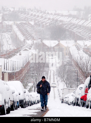 Uomo a camminare su per la collina in tempesta di neve sul modo di lavorare. Foto Stock