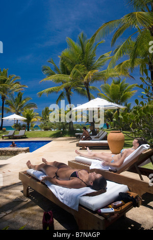 Le giovani donne a prendere il sole sulle sdraio accanto alla piscina nei giardini dell'hotel in Brasile Foto Stock