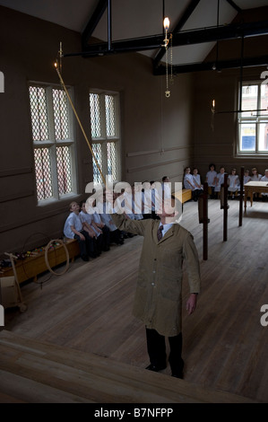 Bambini esperienza di vita in una scuola vittoriana. Un uomo accende una lampada gads in un'aula. Foto Stock