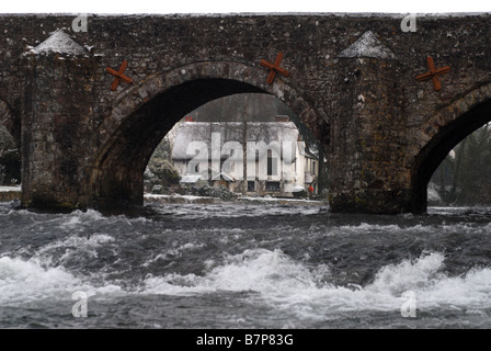 Un insolito panorama di riverside cottage in Bickleigh attraverso un arco sul famoso ponte su acque agitate in Devon Foto Stock