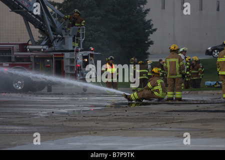 Vigili del fuoco a turno seduto sul tubo flessibile, la spruzzatura di acqua all'interno di un edificio per aiutare a spegnere le fiamme. Foto Stock