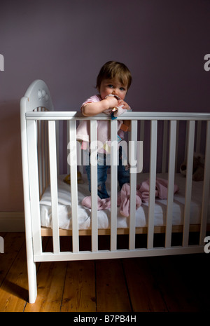 La bambina si alza nella sua culla e mastica sulla sua coperta di comfort Foto Stock