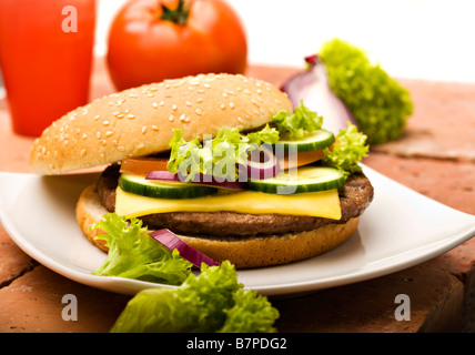 Appena sfornati cheeseburger con pomodoro, cipolla, lattuga, cetriolo in sesame bun su una piastra Foto Stock