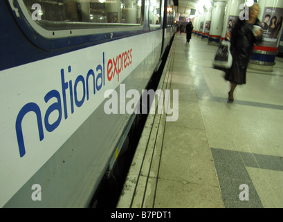 Una donna cammina davanti a un National Express East Anglia con il treno alla stazione di Liverpool Street Foto Stock
