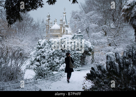 Una giovane donna cammina attraverso la coperta di neve giardini del Royal Pavilion in Brighton la mattina presto. Foto Stock