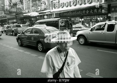 Il vecchio uomo che cammina sulla strada accanto a traffico pesante lungo Thanon Yaowarat in Chinatown Bangkok in Thailandia Foto Stock