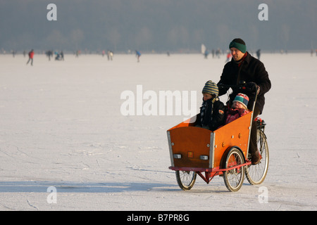 Uomo in camicia nera escursioni in bicicletta con i bambini sulla superficie del ghiaccio congelato Kralingse inverno lago di Rotterdam Paesi Bassi Foto Stock