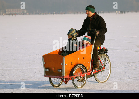 Uomo in camicia nera escursioni in bicicletta con i bambini sulla superficie del ghiaccio congelato Kralingse inverno lago di Rotterdam Paesi Bassi Foto Stock