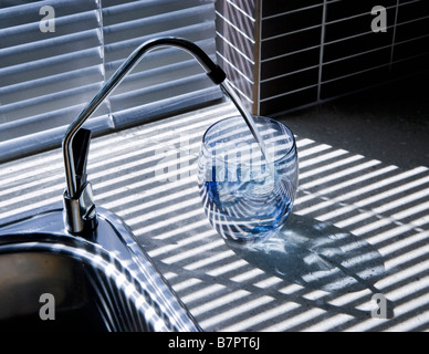 Acqua filtrata versando in un bicchiere da un dissipatore sotto il filtro dell'acqua sistema con il rubinetto sul lato di un lavello da cucina. Foto Stock