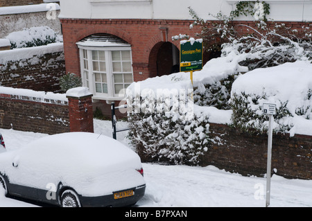 Casa suburbana e auto coperti di neve e venduto segno London REGNO UNITO Foto Stock