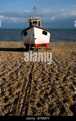 Una spiaggiata barca da pesca elaborata sulla spiaggia di ciottoli sulla battigia Dungeness nel Kent Foto Stock