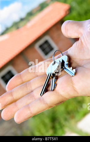 S Man mano che tiene i tasti con una casa in costruzione in background Foto Stock