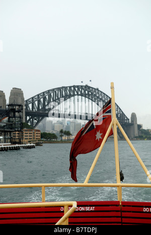 Red Ensign sorvolano top deck posti a sedere e ringhiera del Sydney Harbour Ferry di Sydney Harbour Bridge in background. Foto Stock