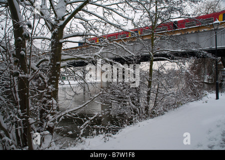 Un treno passa sul Fiume Tamigi a Staines, con la strada alzaia e alberi sotto la neve Foto Stock