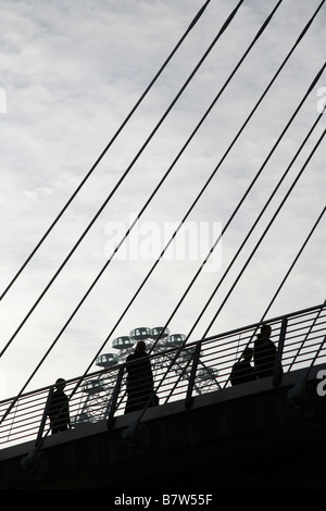 Pedoni stagliano contro London Eye passeggiando attraverso il Golden Jubilee passerella Victoria Embankment, Londra Foto Stock