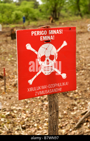 Cranio e crossbones e 'drabbia mine' avviso in portoghese e shangaan su un segno sul bordo di un campo minato in Mozambico. Foto Stock