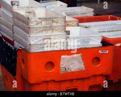 Piccolo vuoto bianco in plastica corrugato contenitori postali impilati in grandi rinforzato arancio bidoni in plastica. Foto Stock