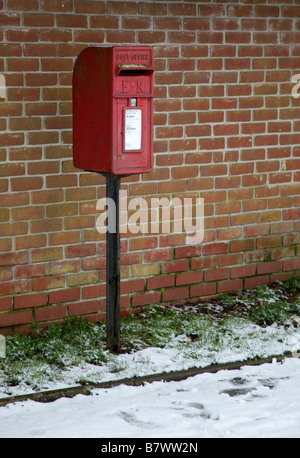 Regno Unito postbox rosso su nero post contro un muro di mattoni nella neve. Remoto villaggio Wiltshire in Inghilterra. Foto Stock