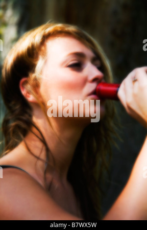 Una giovane donna di bere da un vino rosso bottiglia. Serata di sole. (Soft Focus). Foto Stock