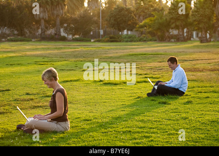 Una coppia moderna social che si distanzia sui loro computer portatili all'esterno in un parco. Foto Stock