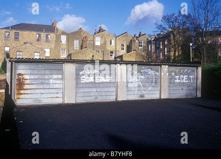 North London scenario urbano fila di quattro lock up garage con graffitti sul metallo porte articolato cantiere dorsi di case Foto Stock