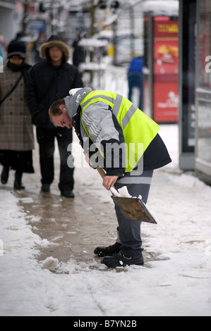 Un lavoratore del consiglio spalare la neve da una trafficata zona pedonale high street Foto Stock