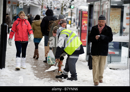 Un lavoratore del consiglio spalare la neve da una trafficata zona pedonale high street Foto Stock