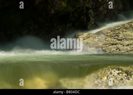 Acqua rotolando giù da e tra rocce e massi in un fiume di acqua di fusione Foto Stock